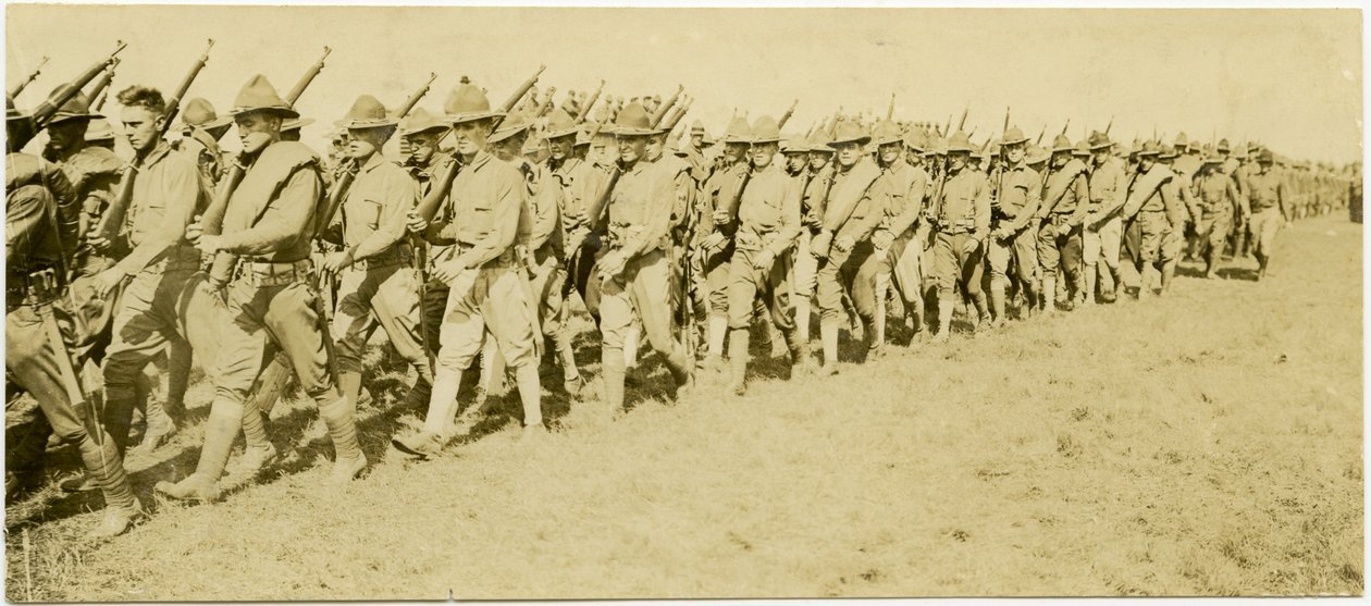 Horizontal, sepia photograph showing rows of uniformed soldiers marching through a grass field  in formation while carrying rifles by Carl Michel