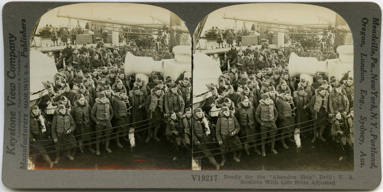 Bir geminin güvertesinde ayakta ve otururken can yelekleri giyen üniformalı Amerikan askerlerini gösteren yatay, sepya stereokart. Keystone Stereograf numarası V19217. başlık okur by Keystone View Company