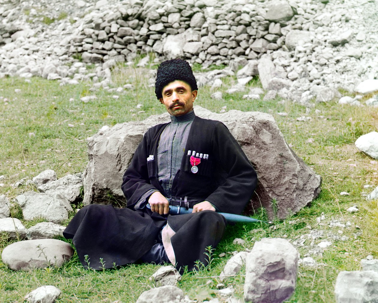 Dağıstanlı tipler - Geleneksel elbise ve başlık giyen Sünni Müslüman adam, yanında kılıflı bir hançer ile yerde oturuyor, Rus İmparatorluğu, 1905 ve 1915 yılları arasında by Sergey Prokudin Gorsky